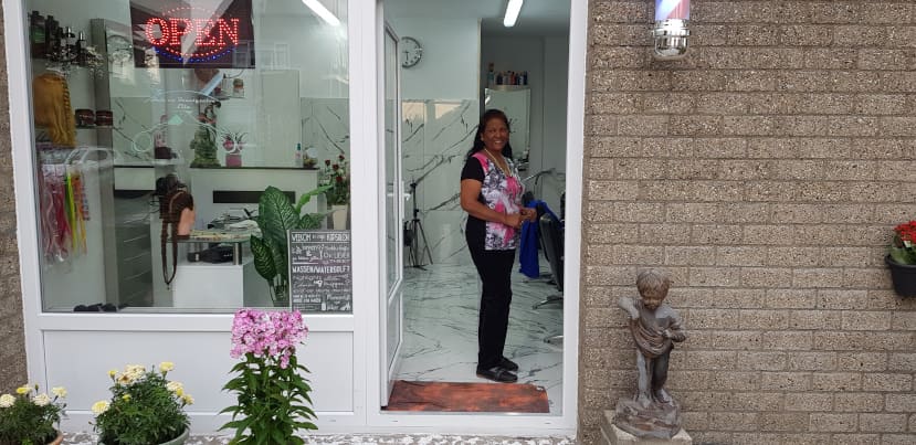 De voorkant van Hair- & Beautysalon Lila aan de Goudseweg, met bloemen bij de deur en een verlicht OPEN-bord in de ruit
