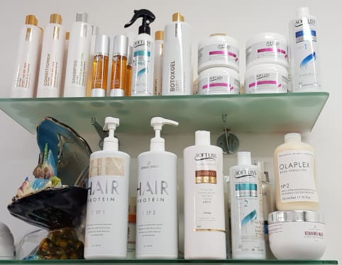 Flessen en potten met haarverzorgingsproducten op een glazen plank in de salon